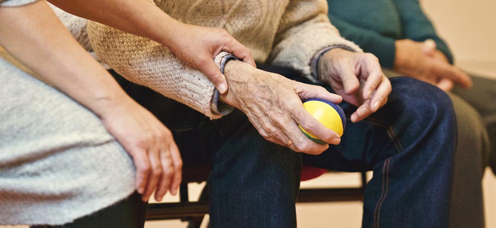 Close up of elderly person's hands holding a ball and being helped by a carer