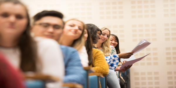 A row of students in a lecture hall, with some smiling and interacting with each other.
