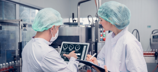 Two people wearing protective clothing and working at a food factory