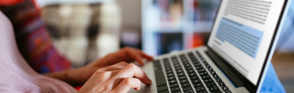 Close up of a student's hand resting on their laptop with a word document open on screen and a paragraph selected