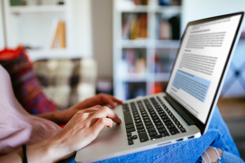 Close up of a student's hand resting on a laptop with a word document on screen