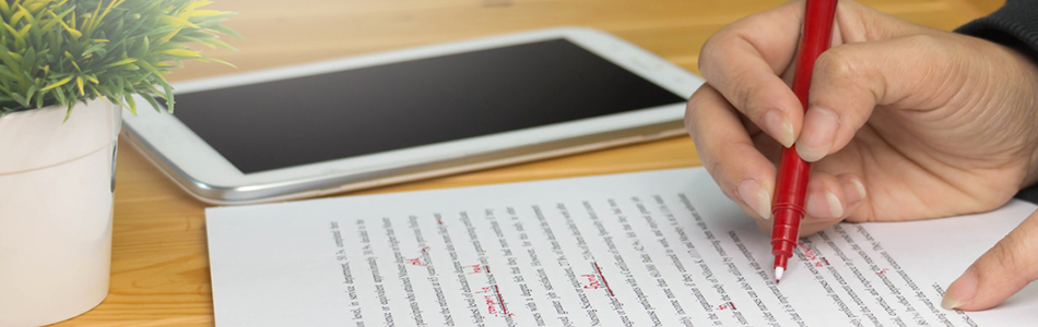 Close up of a hand holding a red pen and proofreading a printed document