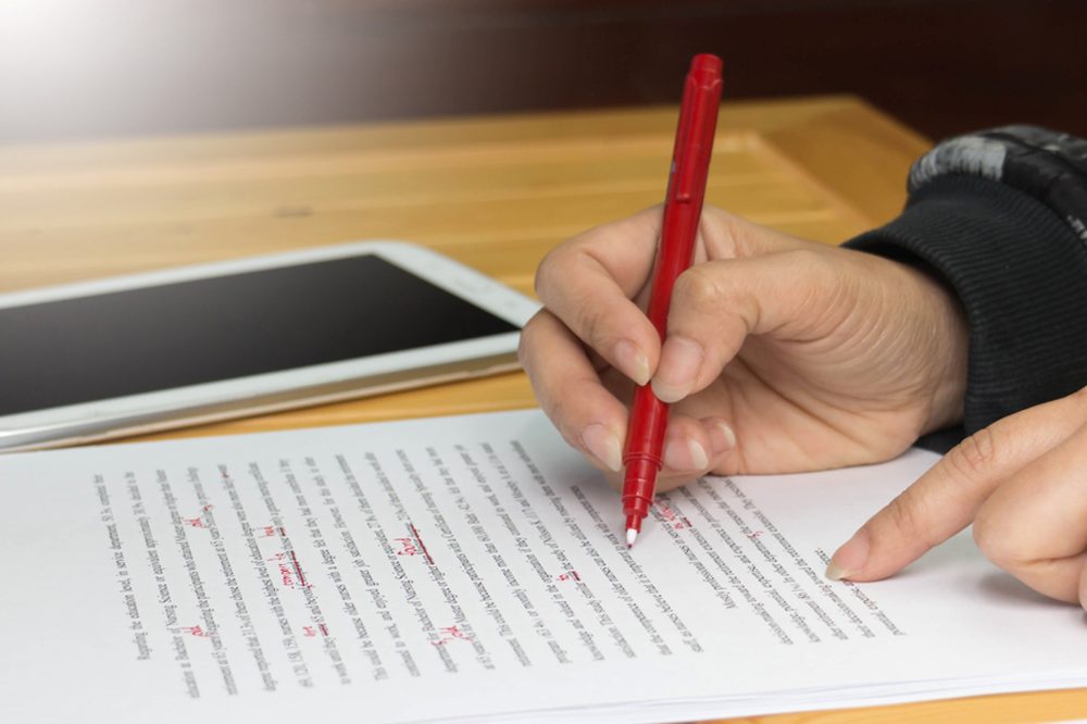 Close up of a hand holding a red pen and proofreading a printed document