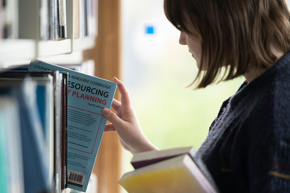 Student picking up a book from the library shelf