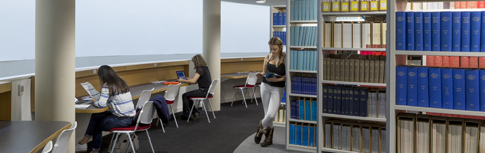 Student reading a book next to the library shelves