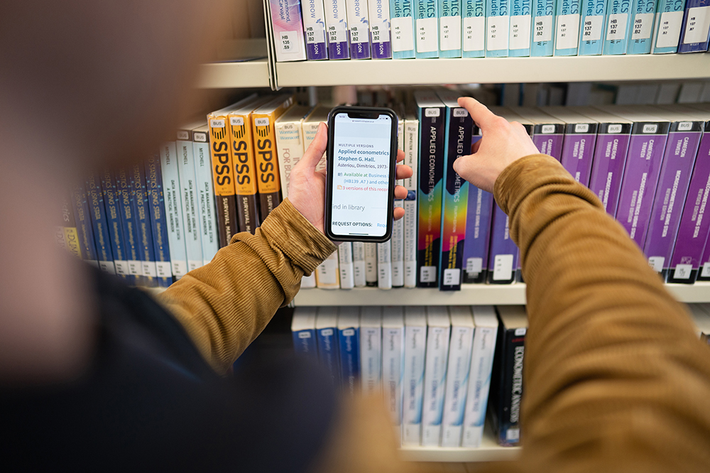 Person using a phone to find a book in the library