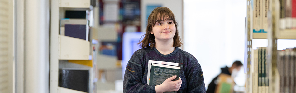 Student using a phone to find books on the library shelves