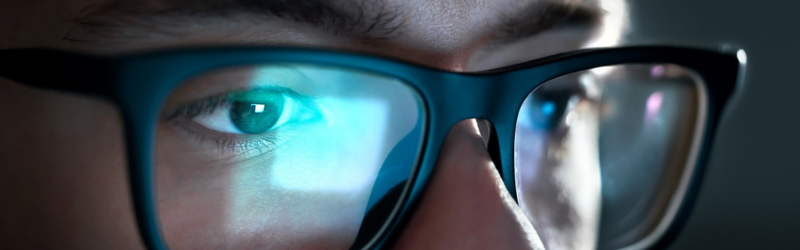 Close up image of a person wearing glasses with the a screen reflected in the glasses