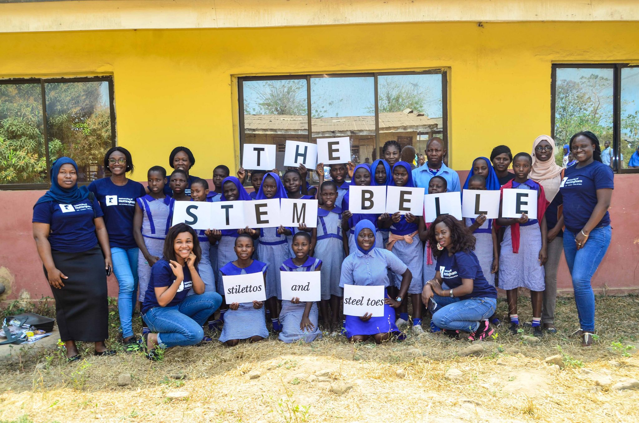 A group of young girls posing posing for a photo and holding up a sign that reads the stem belle stilettos and steel toes