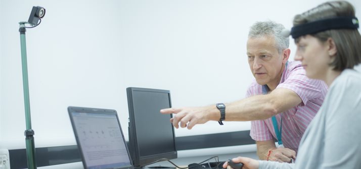 A woman wearing a brain imaging device and looking at a computer next to a man pointing to the computer